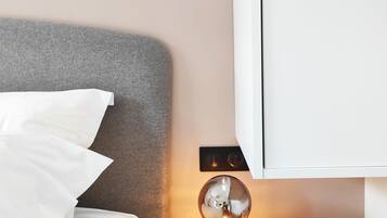 A neatly made bed with white linens, a bedside table with a book, a lamp, and a wardrobe in a bedroom.