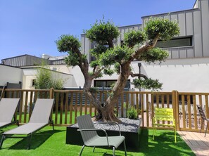 Un espace extérieur moderne doté d’un grand arbre, d’une terrasse en bois et de coins salon extérieurs.