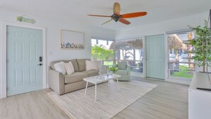 Un salón con un sofá color beige, una mesa de centro blanca y un ventilador de techo.