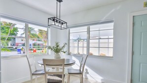 Una habitación luminosa con una mesa redonda y sillas, ventanas amplias y una puerta.