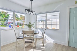 Um quarto claro com uma mesa redonda e cadeiras, janelas amplas e uma porta.