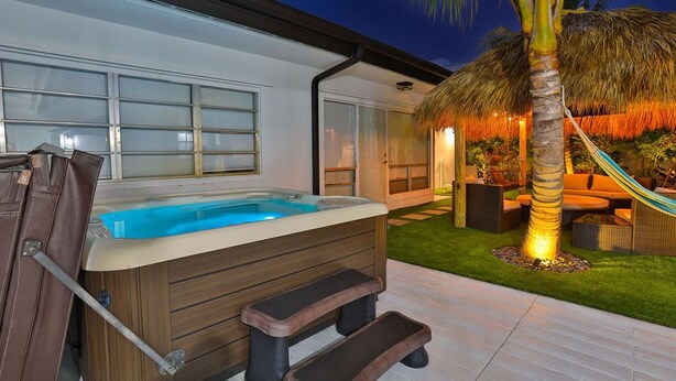 Un jacuzzi con escalones, una palmera y una estructura de techo de paja.