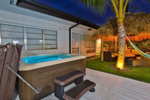 Un jacuzzi con escalones, una palmera y una estructura de techo de paja.