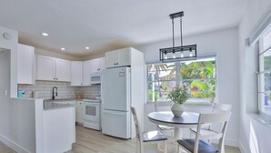 Una cocina moderna con armarios blancos, una isla central y un comedor con mesa y sillas.