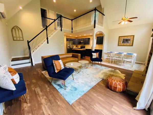 Cozy living area with a high ceiling, sofa, coffee table, and ottoman, leading to an upper level.
