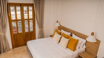 A neatly arranged bedroom with a large bed, wooden headboard, two bedside tables with lamps, and a wooden door with glass panels.