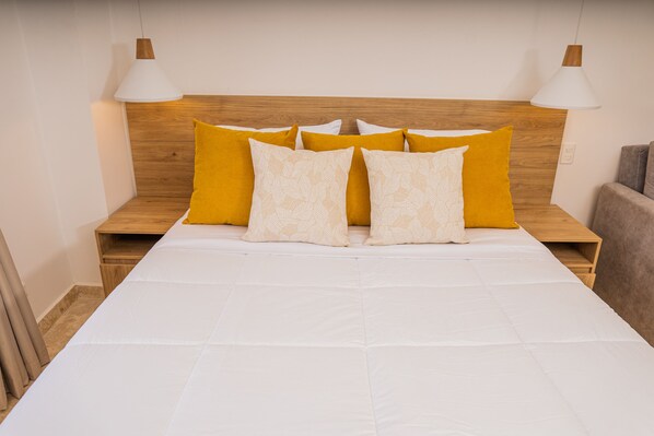 A neatly made bed with white bedding and multiple pillows, including yellow and patterned ones.