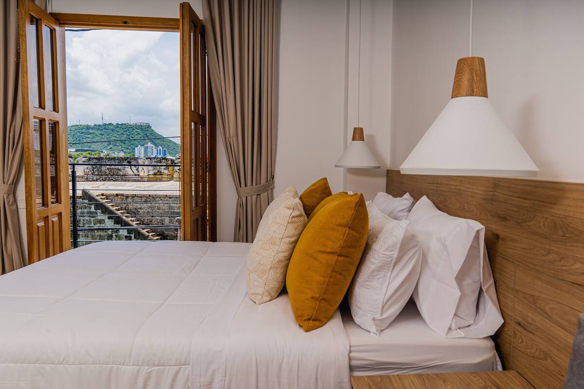 Habitación de hotel con cama, vistas a la ciudad, cabecero de madera y lámpara blanca.