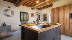 Una cuina moderna amb una illa central, bigues de fusta, un rellotge i una finestra.