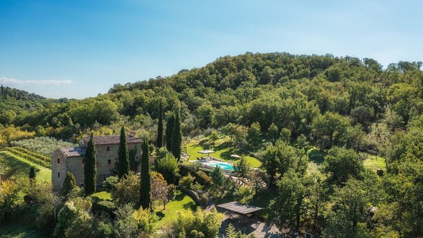 Edifici de pedra envoltat de vegetació exuberant i piscina.