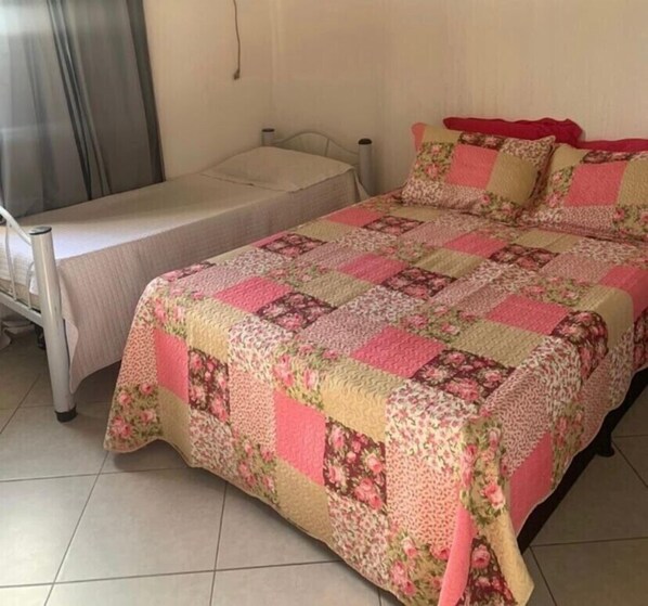 A single bed with a floral quilt, a bedside table, and a window with curtains.
