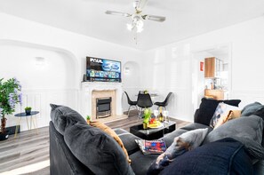 A modern living room with a fireplace, a flat-screen TV, and a ceiling fan.