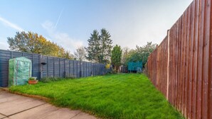 A backyard with a wooden fence, a green lawn, and a concrete path.