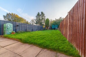 A backyard with a wooden fence, a green lawn, and a concrete path.
