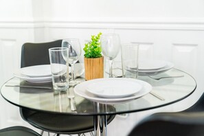 A round glass table with white plates, clear glasses, and a small wooden vase with a green plant.