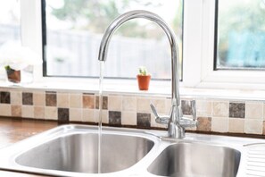 A kitchen sink with a running faucet, a window with a view of greenery, and a tiled backsplash.