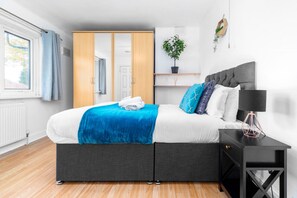 A modern bedroom with a grey bed, white and blue bedding, a black nightstand, and a potted plant on a shelf. - Luxury 3 Bed House -  Garden - Parking (Birmingham)