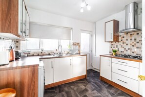 A modern kitchen with white cabinets, a wooden countertop, a stainless steel range hood, and a tiled backsplash. - Luxury 3 Bed House -  Garden - Parking (Birmingham)