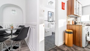 Una cocina moderna con lavadora, un comedor con mesa y sillas redondas, y un baño con espejo y lavamanos.