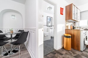 A modern kitchen with a washing machine, a dining area with a round table and chairs, and a bathroom with a mirror and sink.