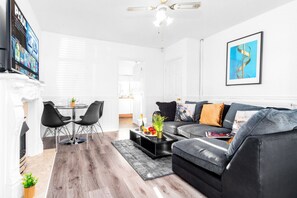 A modern living room with a black leather sofa, a dining table with chairs, a fireplace, and a large TV screen. - Luxury 3 Bed House -  Garden - Parking (Birmingham)