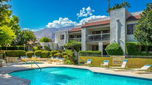 A swimming pool with lounge chairs, a fenced area, and a building with a red-tiled roof. - Top-floor Condo w/Balcony & Mountain Views (Palm Springs)
