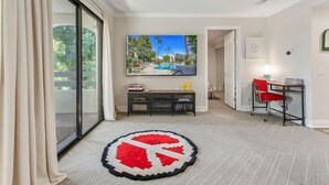 A modern living room with a large TV, a small table, and a red chair. - Top-floor Condo w/Balcony & Mountain Views (Palm Springs)