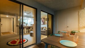 A modern living room with a wooden dining table, a sofa, and a kitchen in the background. - Top-floor Condo w/Balcony & Mountain Views (Palm Springs)