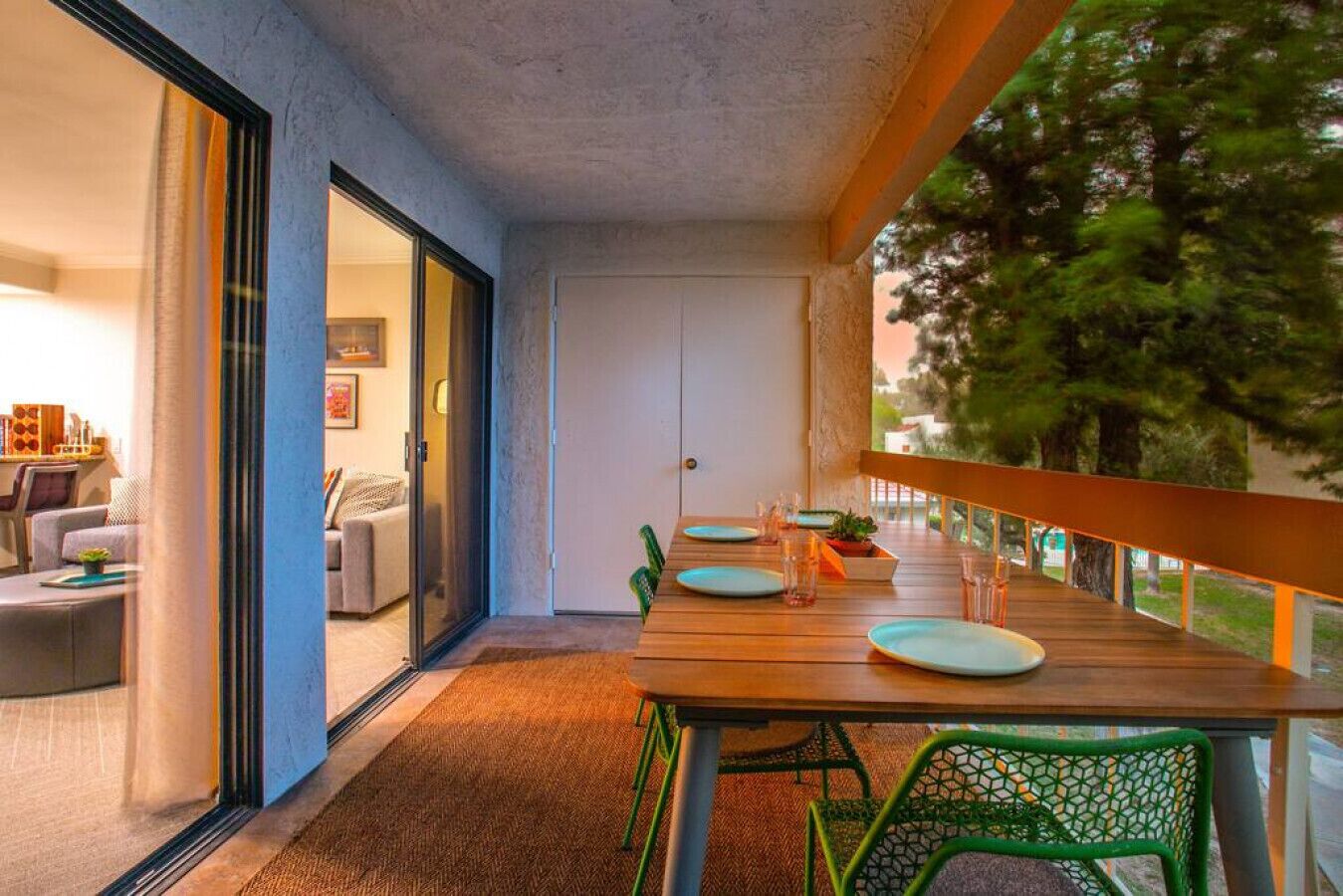 Un balcon avec une table en bois dressée pour le repas, des chaises vertes et une vue sur les arbres.