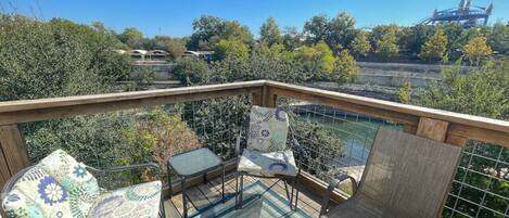 A balcony with three chairs and a table, overlooking a scenic view of trees and a distant bridge.