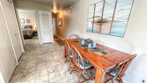 A dining area with a wooden table and chairs, a tiled floor, and a painting on the wall.