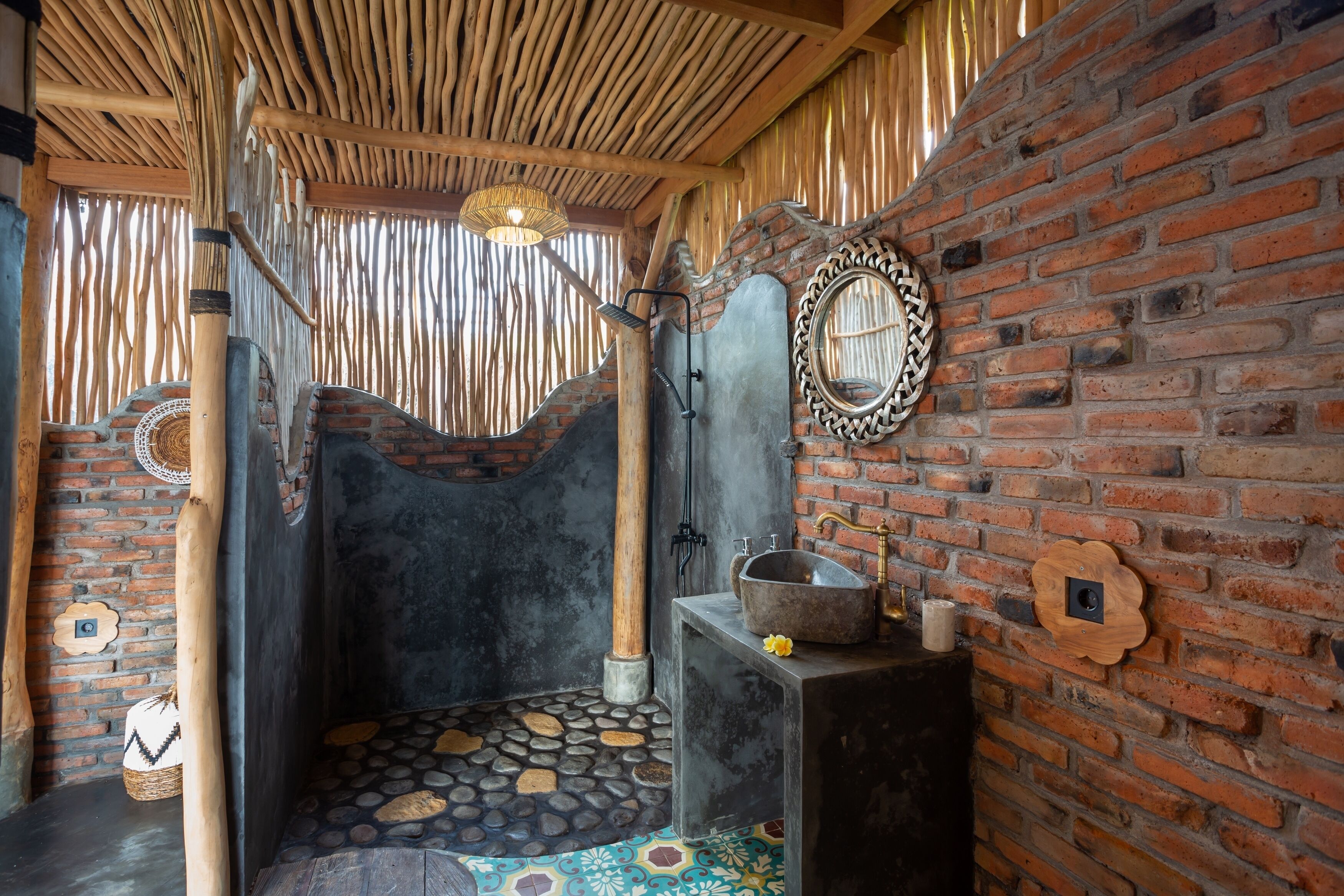 Un baño rústico con pared de ladrillo, un espejo grande, un lavamanos de piedra y techo de madera.