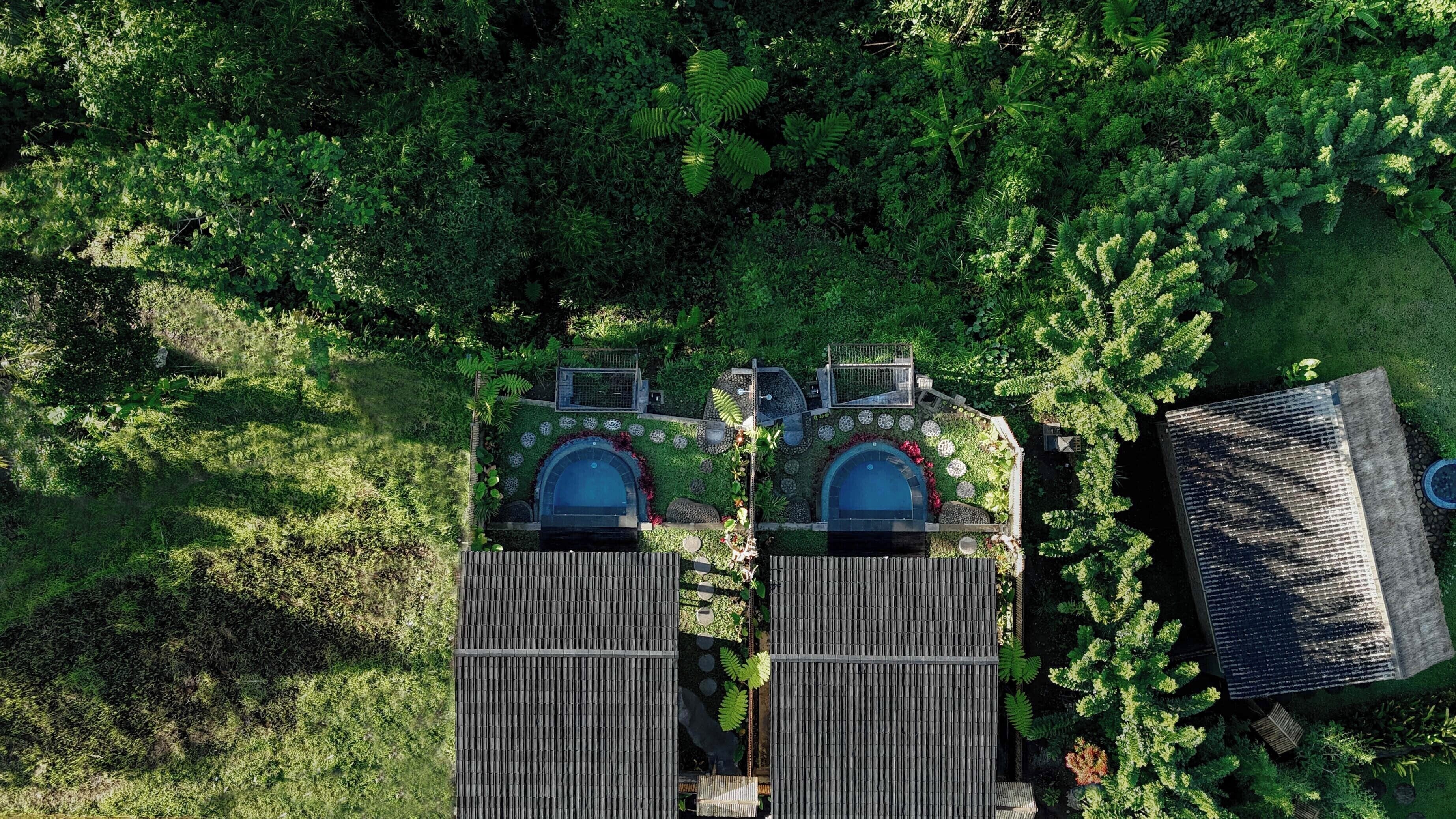 Vista aérea de una propiedad con dos piscinas separadas, rodeada de exuberante vegetación y una terraza de madera.