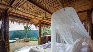 Habitación con cama bajo dosel, suelo de piedra, muebles de mimbre y vistas a zonas verdes.