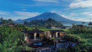 Un resort tropical con arquitectura tradicional, un área de piscina y vista a un volcán al fondo.