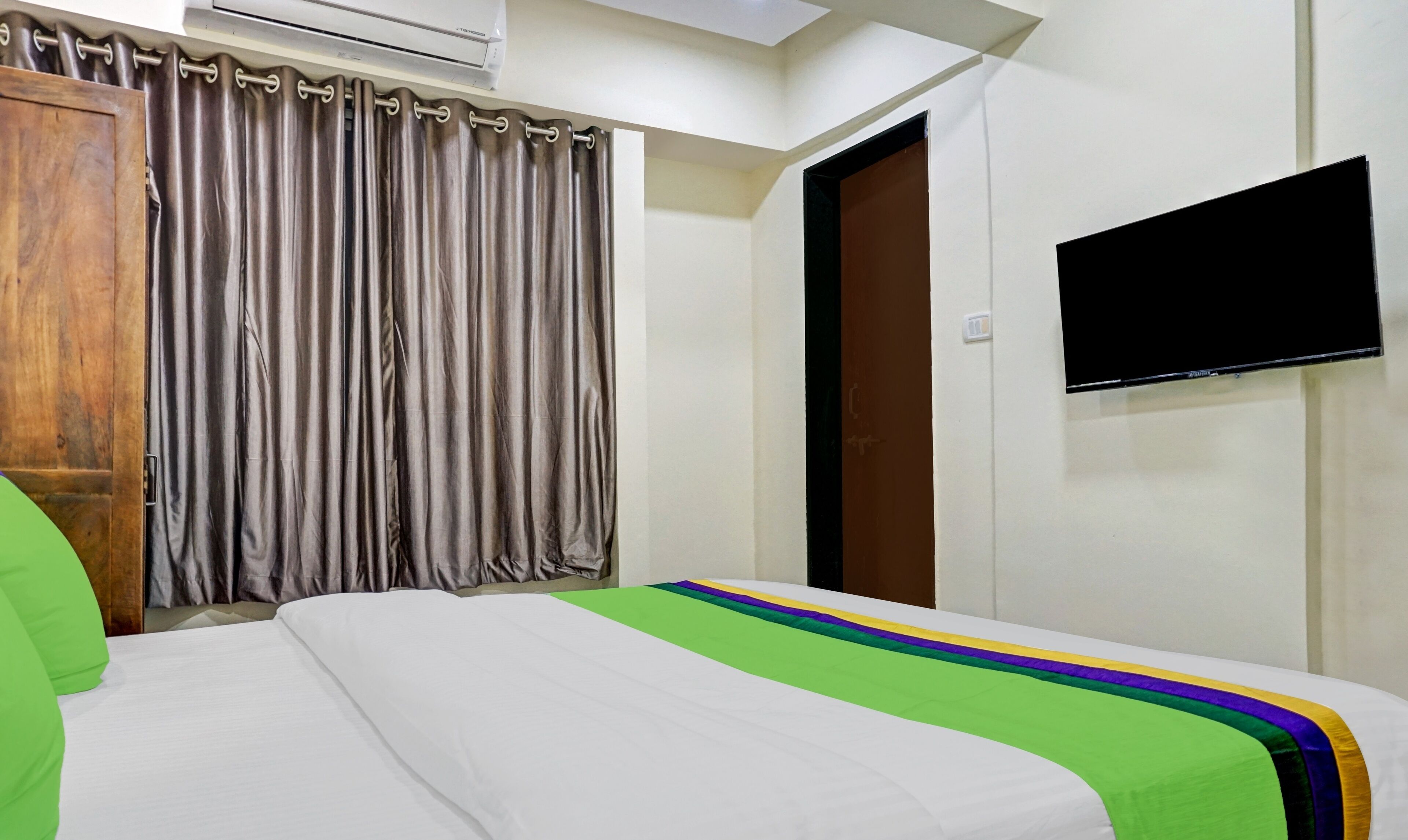 Habitación de hotel con cama, cortinas, televisor y aire acondicionado.