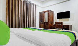 Quarto de hotel com cama, escrivaninha, cadeira, televisão e guarda-roupa.