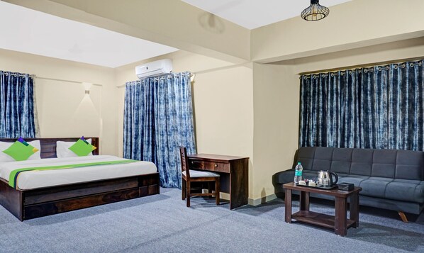 Quarto de hotel com cama, escrivaninha, cadeira, sofá, mesinha e garrafa de água.
