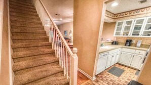 Un escalier menant à une cuisine avec des meubles blancs et un sol en briques.