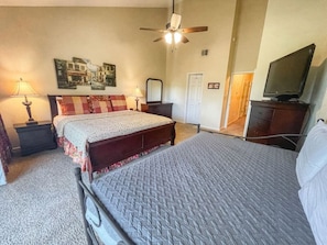 A bedroom with two beds, a ceiling fan, a television, and a door.