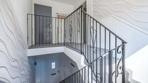 A staircase with a metal railing, a door at the bottom, and a wall with a wavy pattern. - The Douglas  2 Bed Apartment in Uddingston (Uddingston)