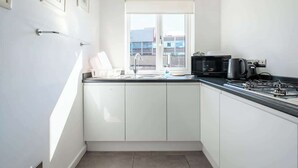 A small kitchen with white cabinets, a black countertop, a window, and a microwave. - The Douglas  2 Bed Apartment in Uddingston (Uddingston)