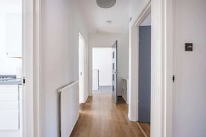 A narrow hallway with white walls and wooden flooring, leading to a door with a blue frame.