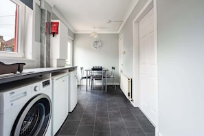 A laundry area with a washing machine, a table with chairs, a clock on the wall, and a window.