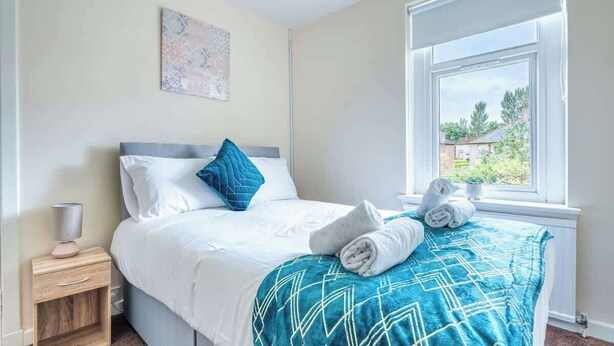A hotel room with a bed, a nightstand, a window with a view, and a painting on the wall. - Millfield House -2 Bed in Motherwell near Motorway (North Lanarkshire)
