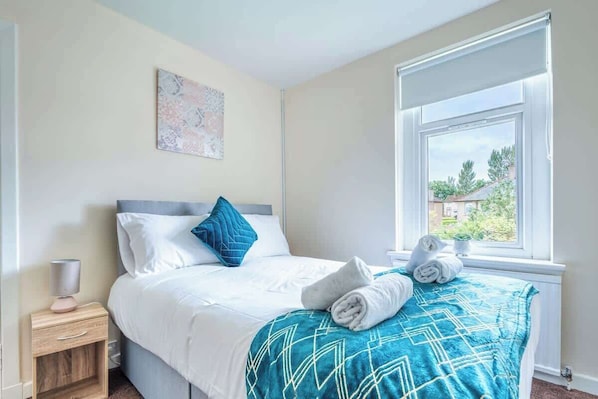 A hotel room with a bed, a nightstand, a window with a view, and a painting on the wall.