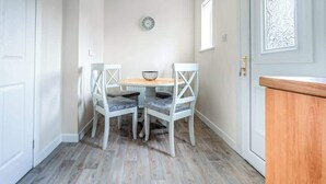 A dining area with a round table and four chairs, a clock on the wall, and a door with a decorative window. - Millfield House -2 Bed in Motherwell near Motorway (North Lanarkshire)