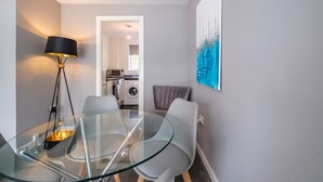 Un soggiorno moderno con un tavolo da pranzo in vetro, una lampada da terra e un dipinto raffigurante un panorama urbano.
