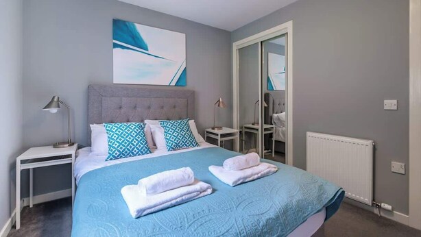 Un letto rifatto con biancheria azzurra, una testiera grigia e un comodino con una lampada.