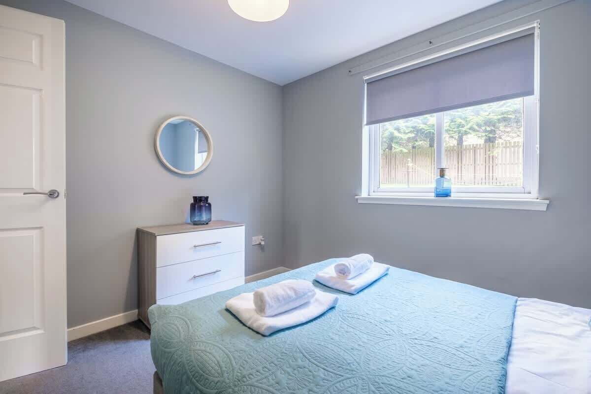 Quarto com cama, penteadeira, espelho e janela com vista para o verde.